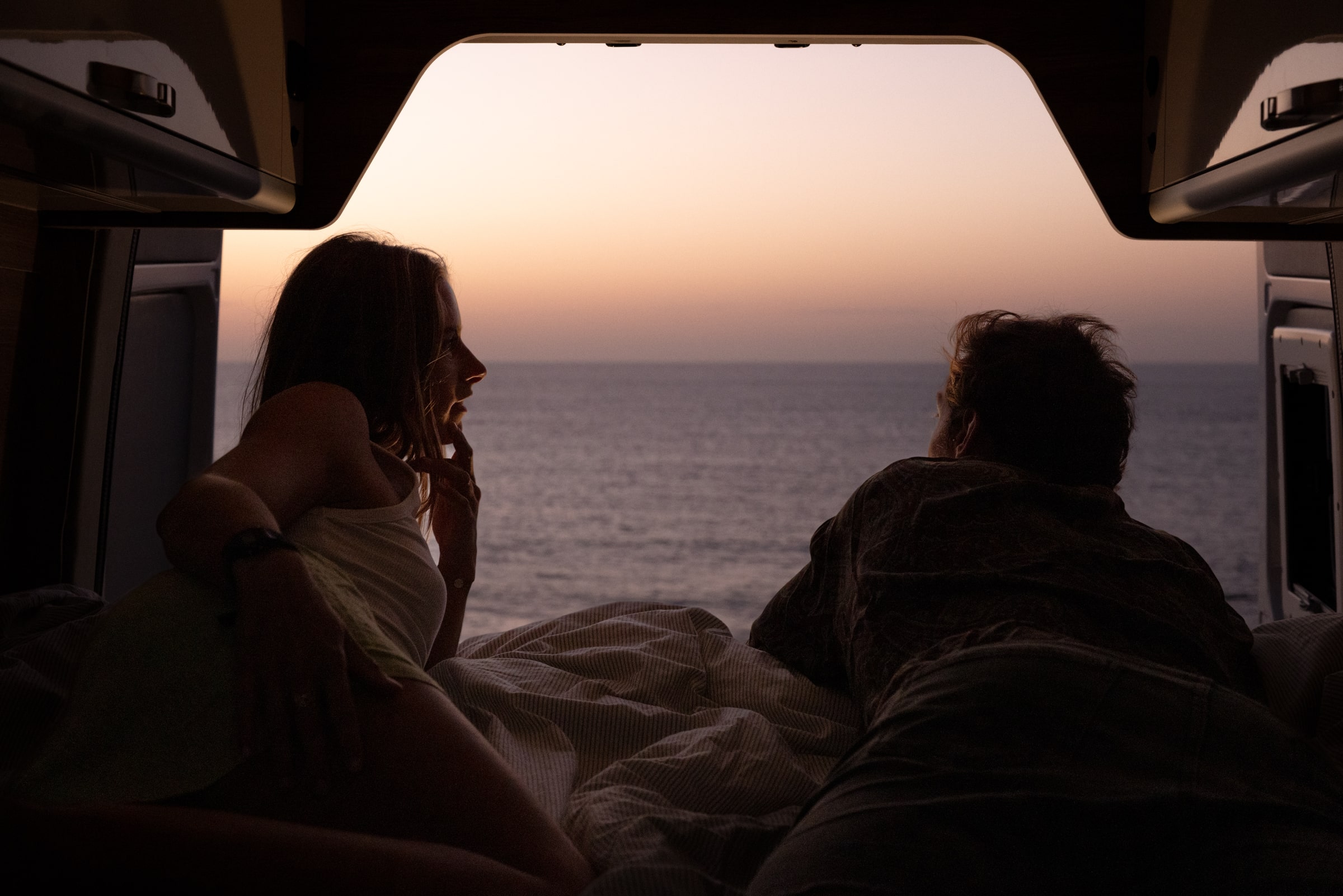 Dormir dans un camping-car aux îles Canaries : un couple contemple le coucher de soleil sur la mer depuis leur lit de camping-car